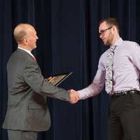 Doctor Potteiger shaking hands with an award recipient with a light lavender shirt and swirl pattern tie